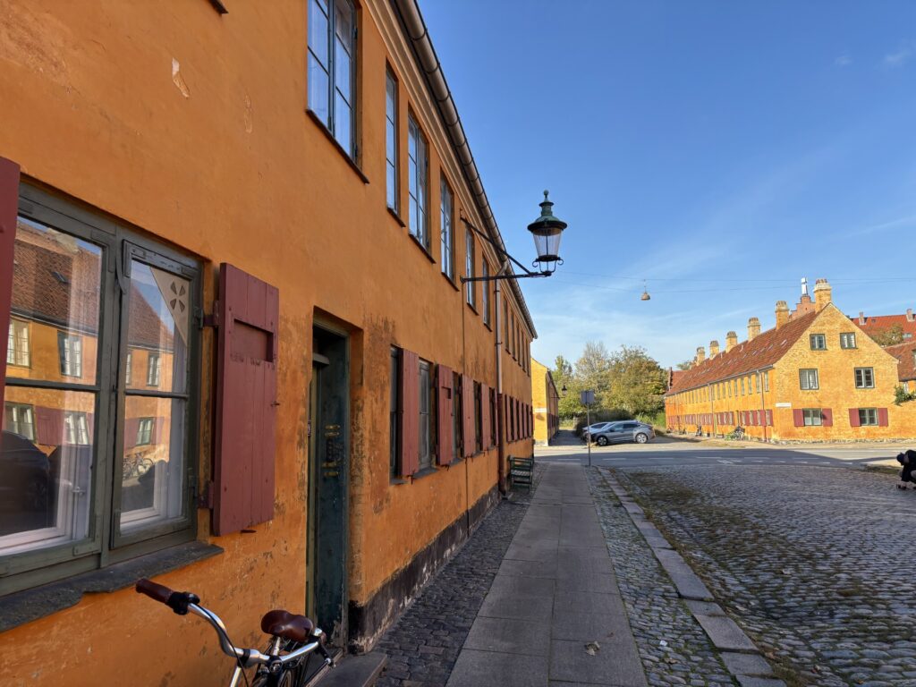 Nyboders okkergule rækkehuse langs en brostensbelagt gade i solskin.