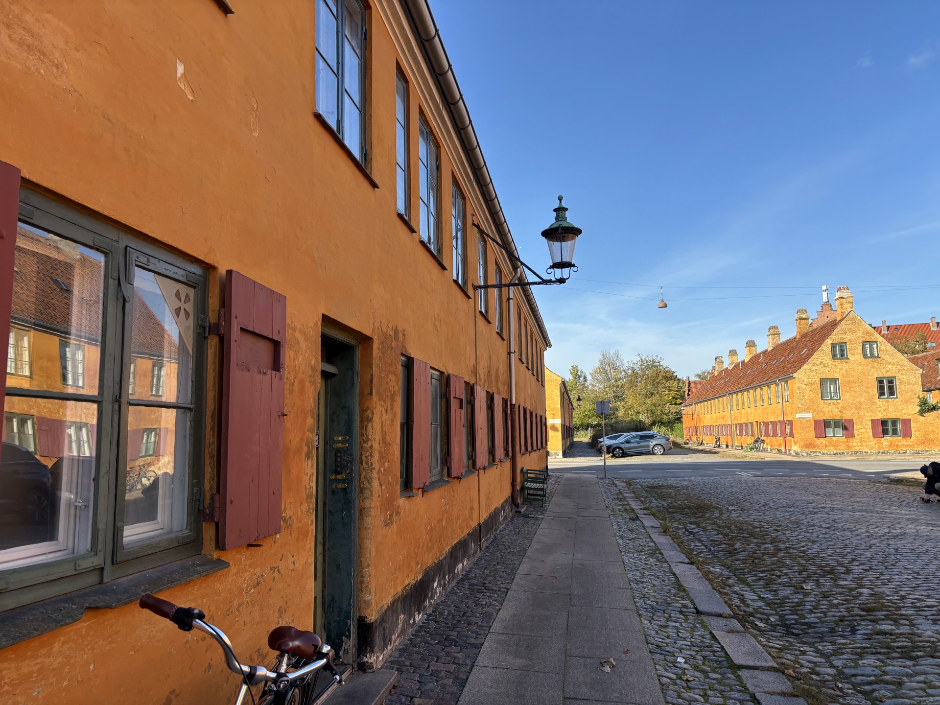 Nyboders okkergule rækkehuse langs en brostensbelagt gade i solskin.