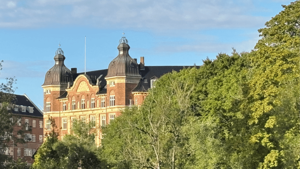 Ældre københavnsk pragtbygning med tårne set gennem træerne.
